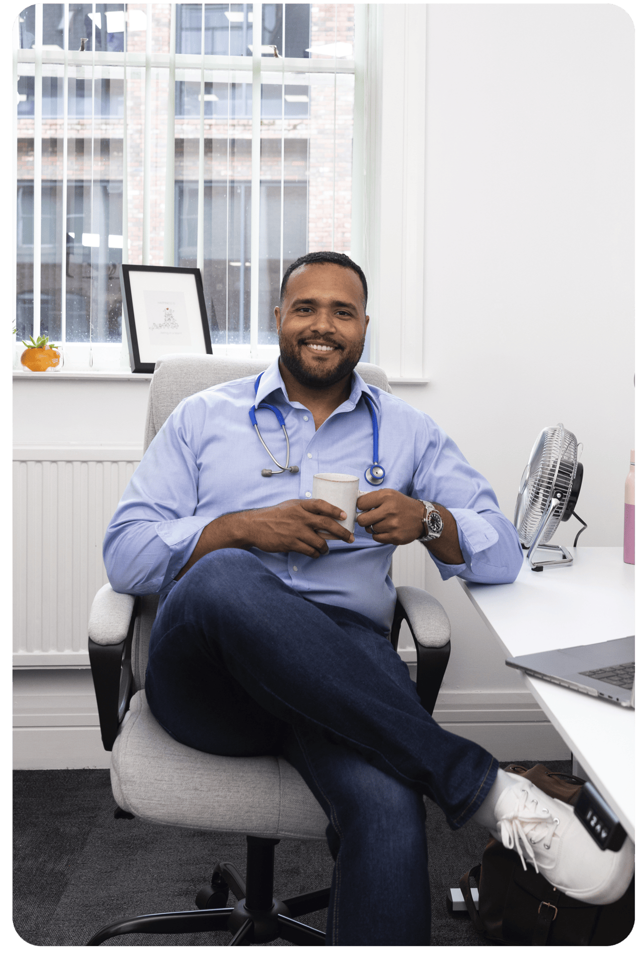 Man sitting in GP consultation room holding coffee, awaiting long-term condition review